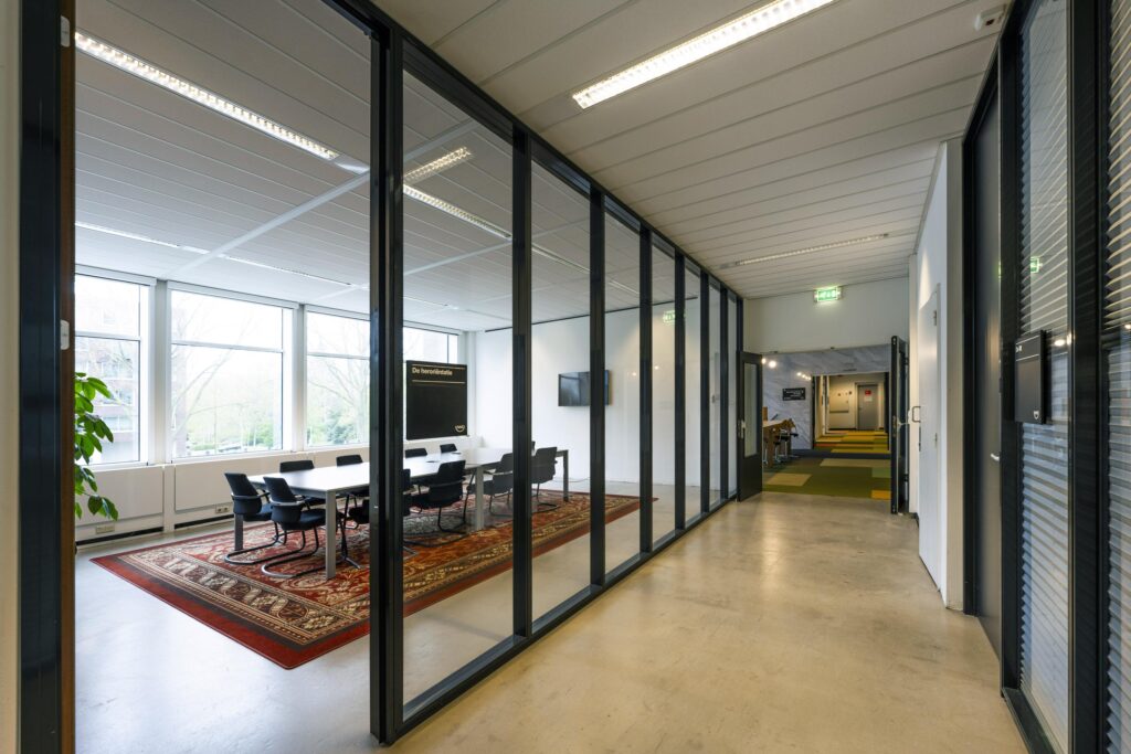 Modern office hallway with glass-walled meeting room at Laan van Kronenburg.